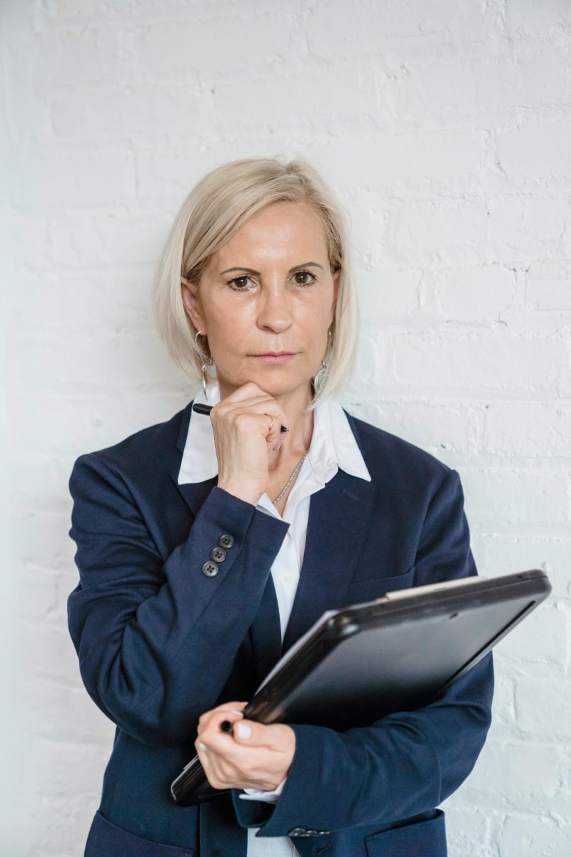 Confident businesswoman with tablet posing against a white brick wall.